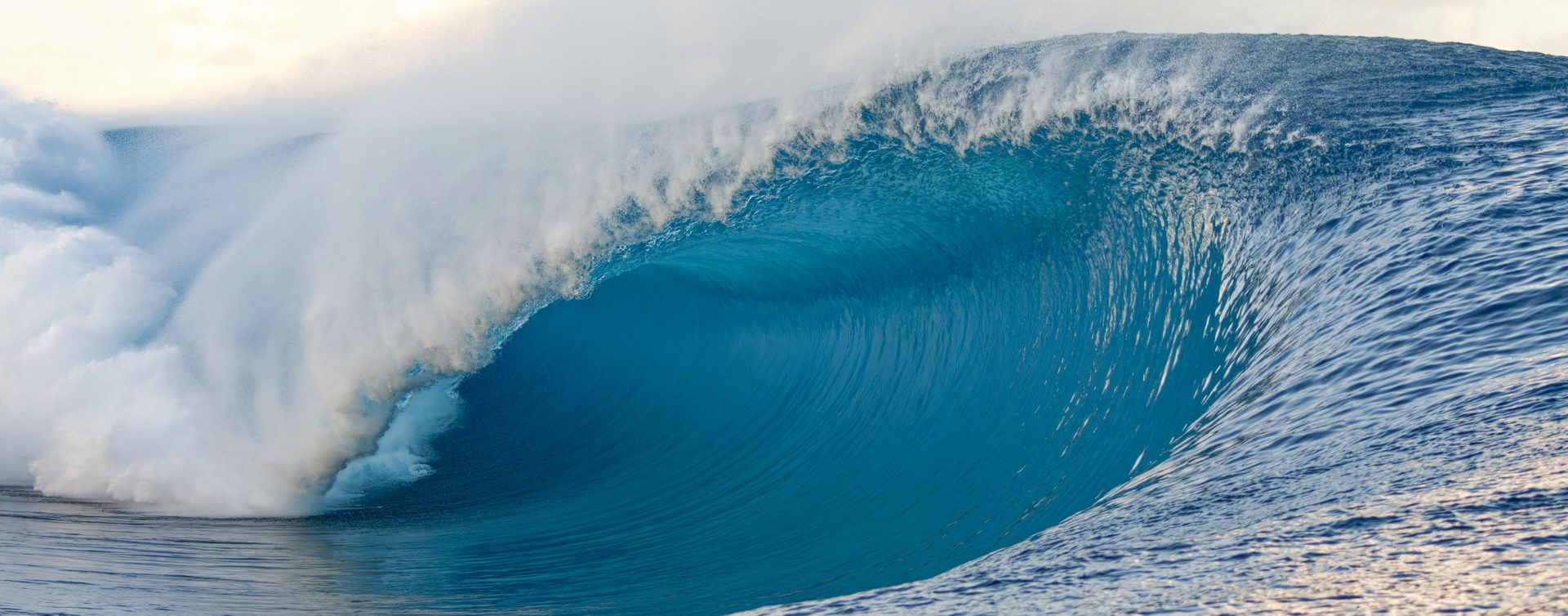A glassy blue-green wave curling over into a barrel under a clear sky
